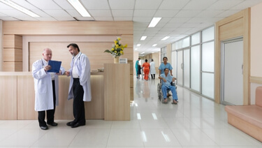 Doctors reviewing a tablet at a hospital reception desk with patients in the hallway